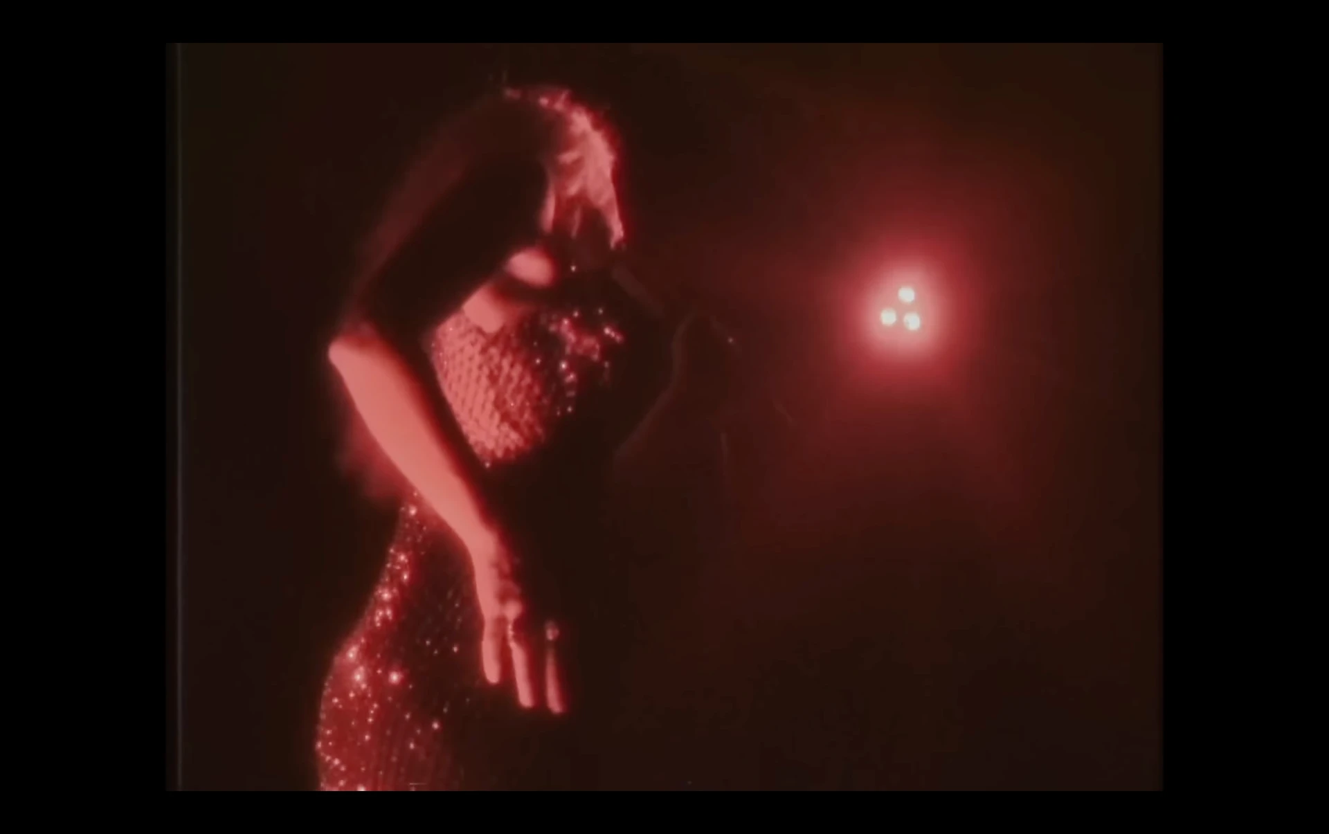 Music video frame of a performer in red stage light