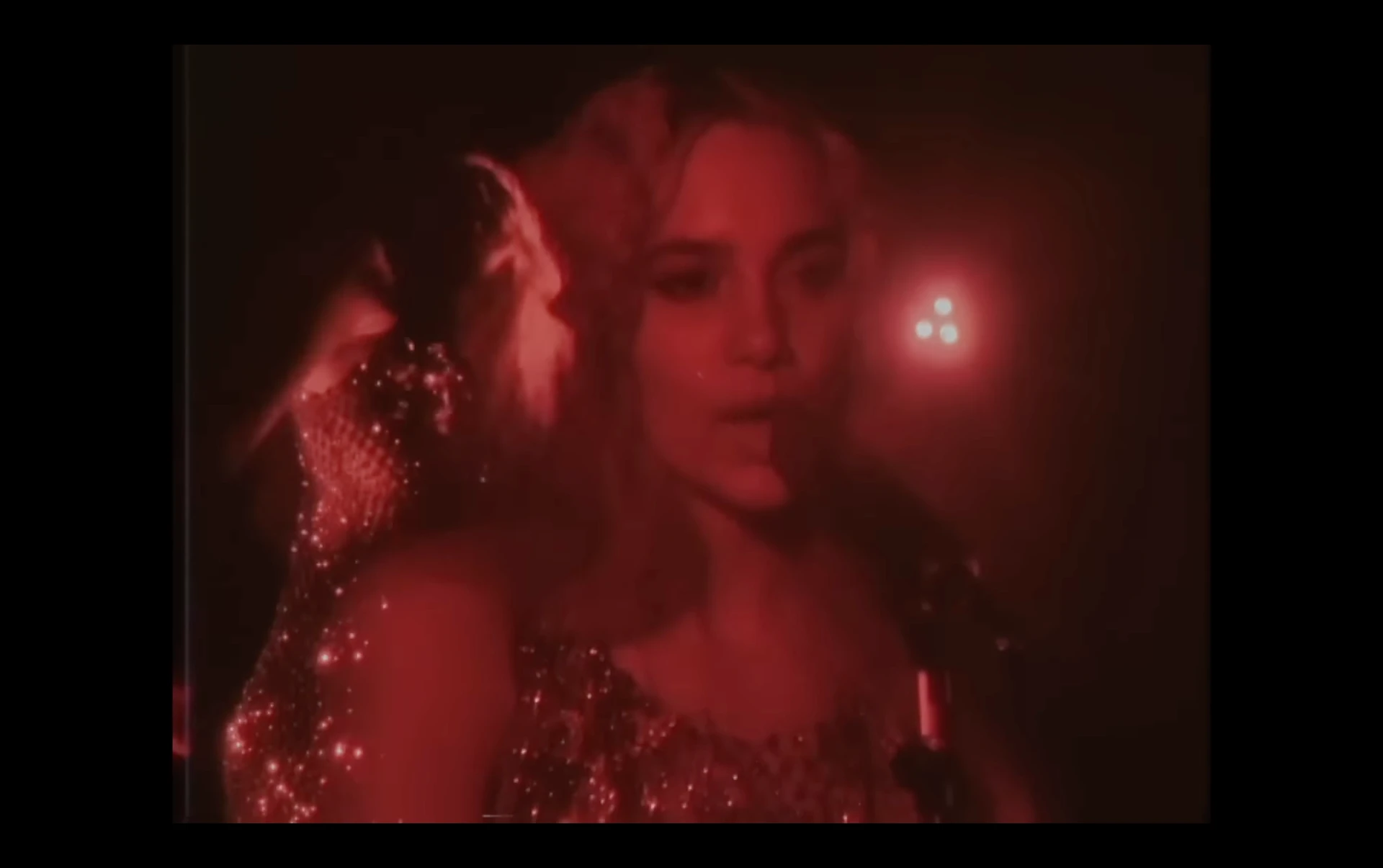 Music video frame with layered performer portraits in red light