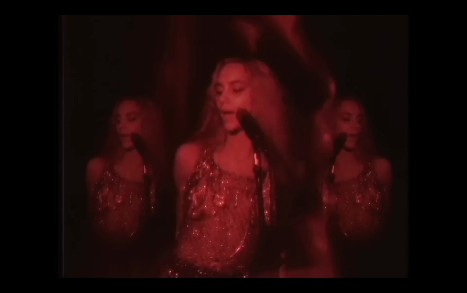 Music video frame of three performers singing in red light